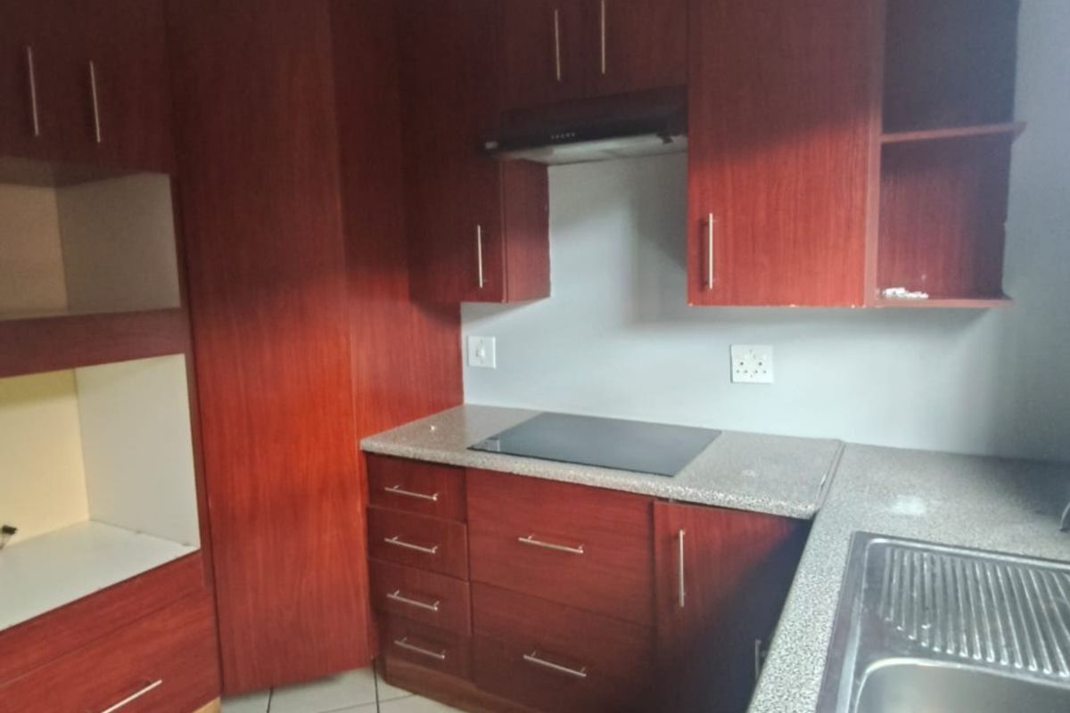 A functional kitchen featuring dark wood cabinetry, granite countertops, a built-in electric hob with extractor fan, and tiled flooring.
