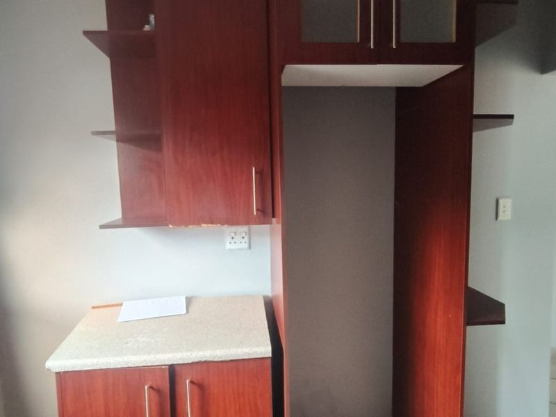 A kitchen area featuring dark wood-finish built-in cabinetry, a dedicated refrigerator alcove, and tiled flooring.