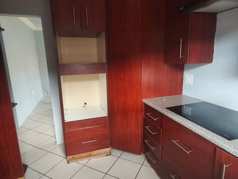 A functional kitchen featuring dark wood cabinetry, granite countertops, and an integrated electric hob, currently vacant and ready for updates.