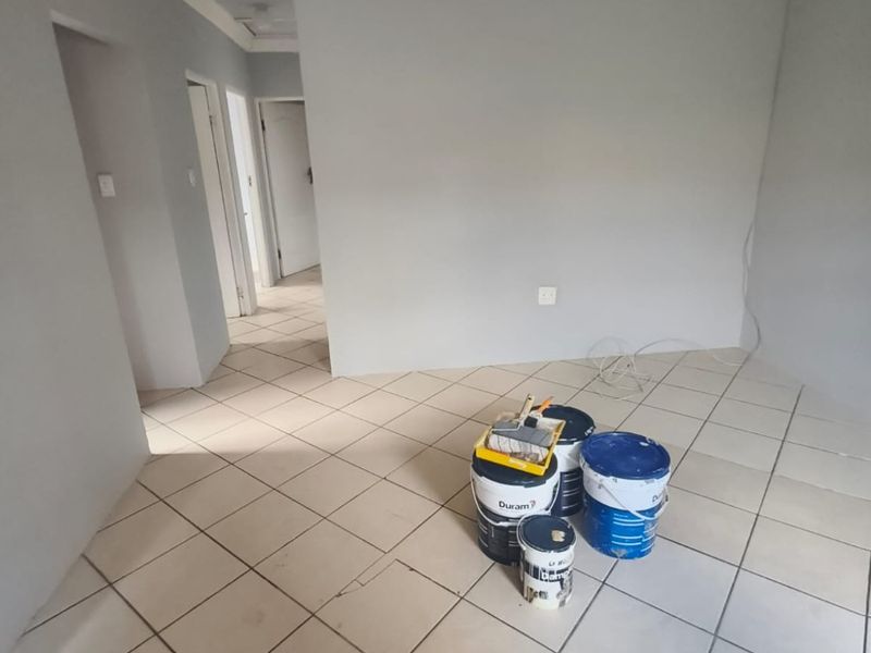An empty living area featuring neutral grey walls, ceramic floor tiles, and decorative ceiling cornicing, currently undergoing minor maintenance.