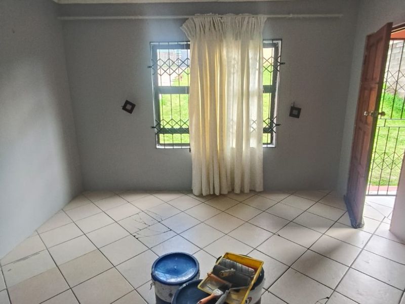 An empty bedroom featuring tiled flooring, decorative ceiling cornices, and security bars on the window, currently undergoing minor maintenance.