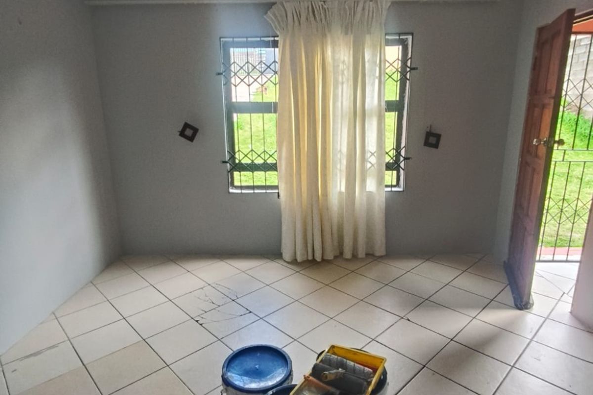 An empty bedroom featuring tiled flooring, decorative ceiling cornices, and security bars on the window, currently undergoing minor maintenance.