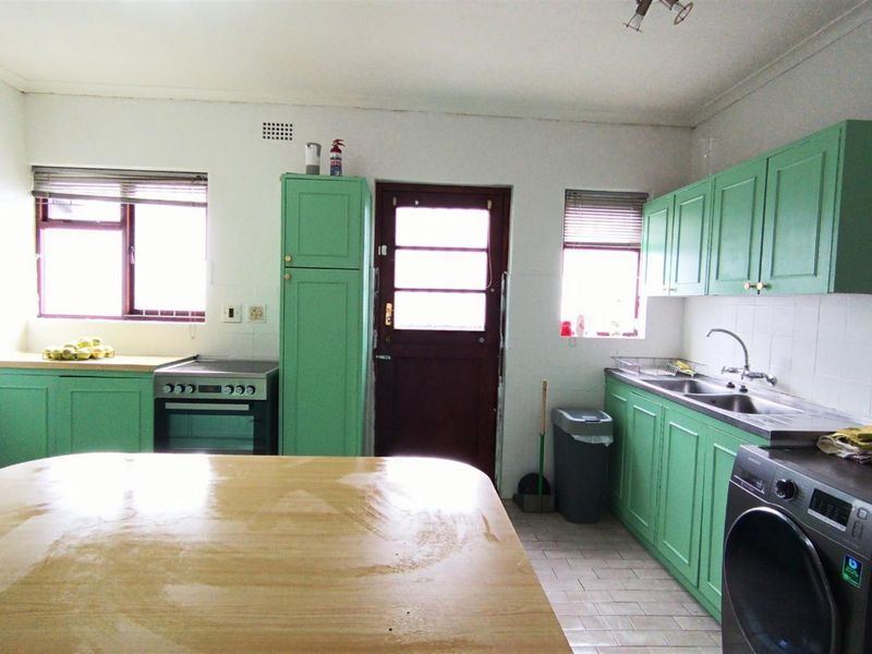 A functional kitchen featuring green cabinetry, a stainless steel sink, tiled backsplash, and a freestanding stove with direct access to the exterior.