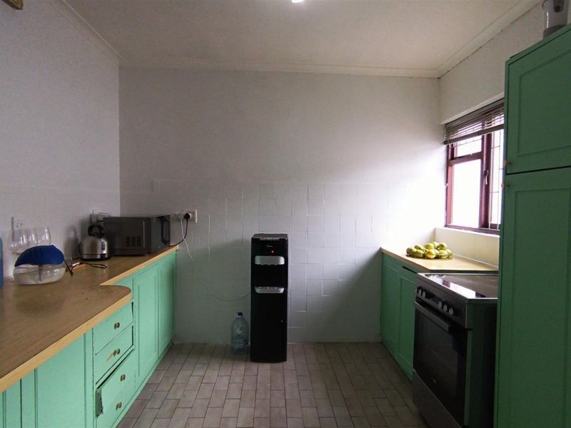 A functional kitchen featuring mint green cabinetry, laminate countertops, tiled backsplash, and a freestanding oven with natural light from the side window.