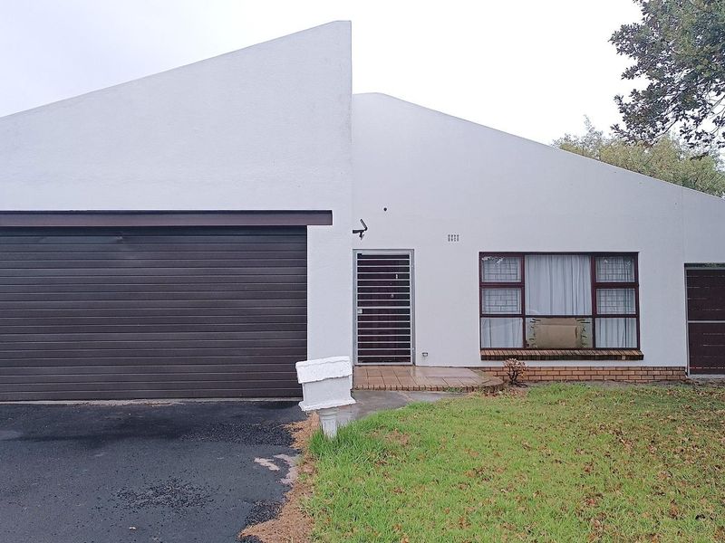 Front elevation of a house featuring a single garage, security gate entrance, and a paved walkway with a small front lawn.