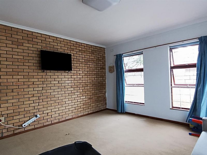 A living room featuring an exposed brick accent wall, carpeted flooring, and large windows that provide natural light.