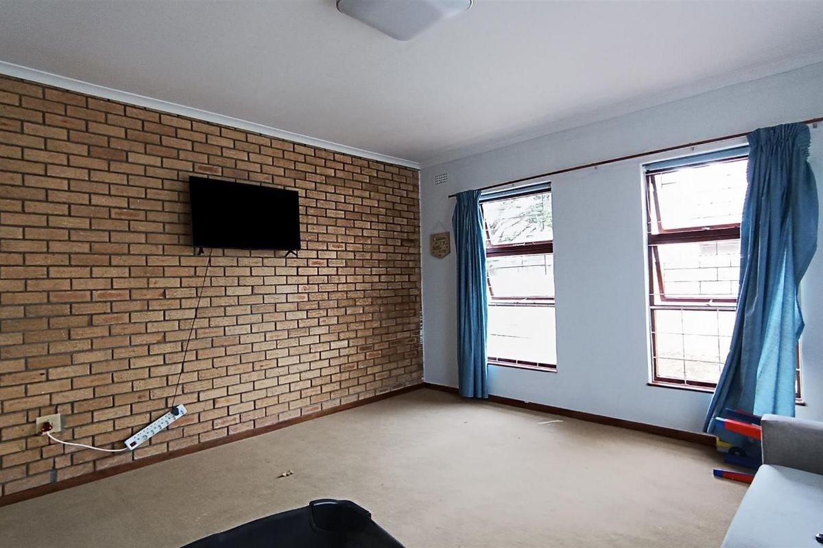 A living room featuring an exposed brick accent wall, carpeted flooring, and large windows that provide natural light.
