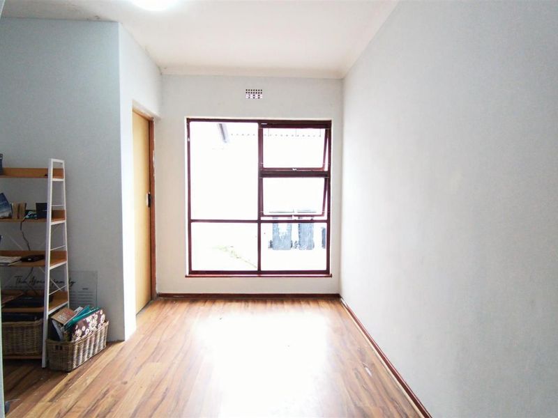 A bright, empty living room featuring laminate flooring, neutral walls, and a large window providing natural light.