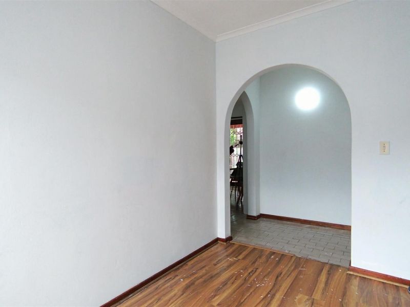 An empty living area featuring an arched doorway leading to an adjacent space, with laminate and tiled flooring throughout.