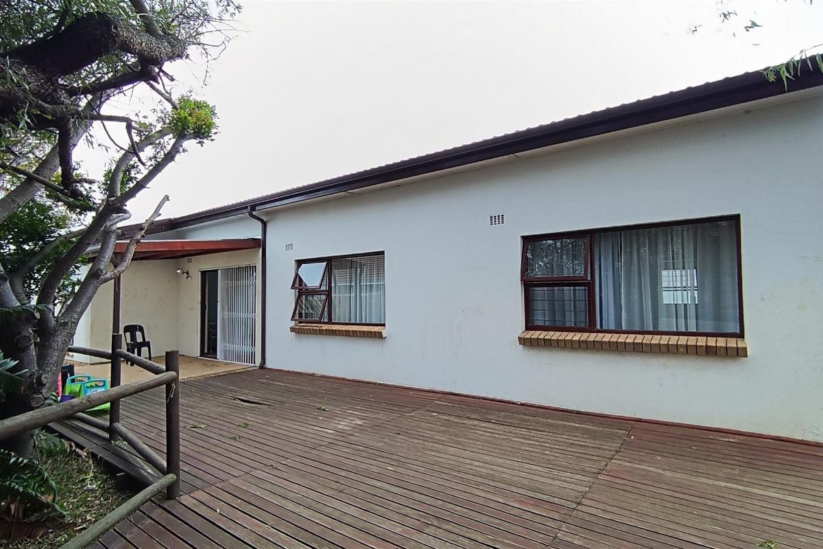 Rear view of the property featuring a large timber deck, covered patio area, and aluminium framed windows with brick sills.
