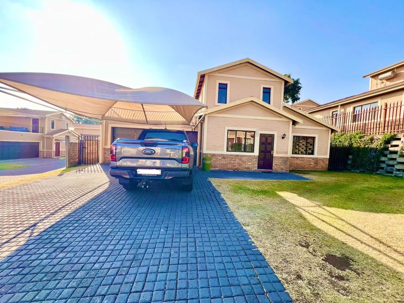 Front elevation of a two-story residential house featuring a paved driveway, shade sail carport, and a well-maintained brick and plaster facade.