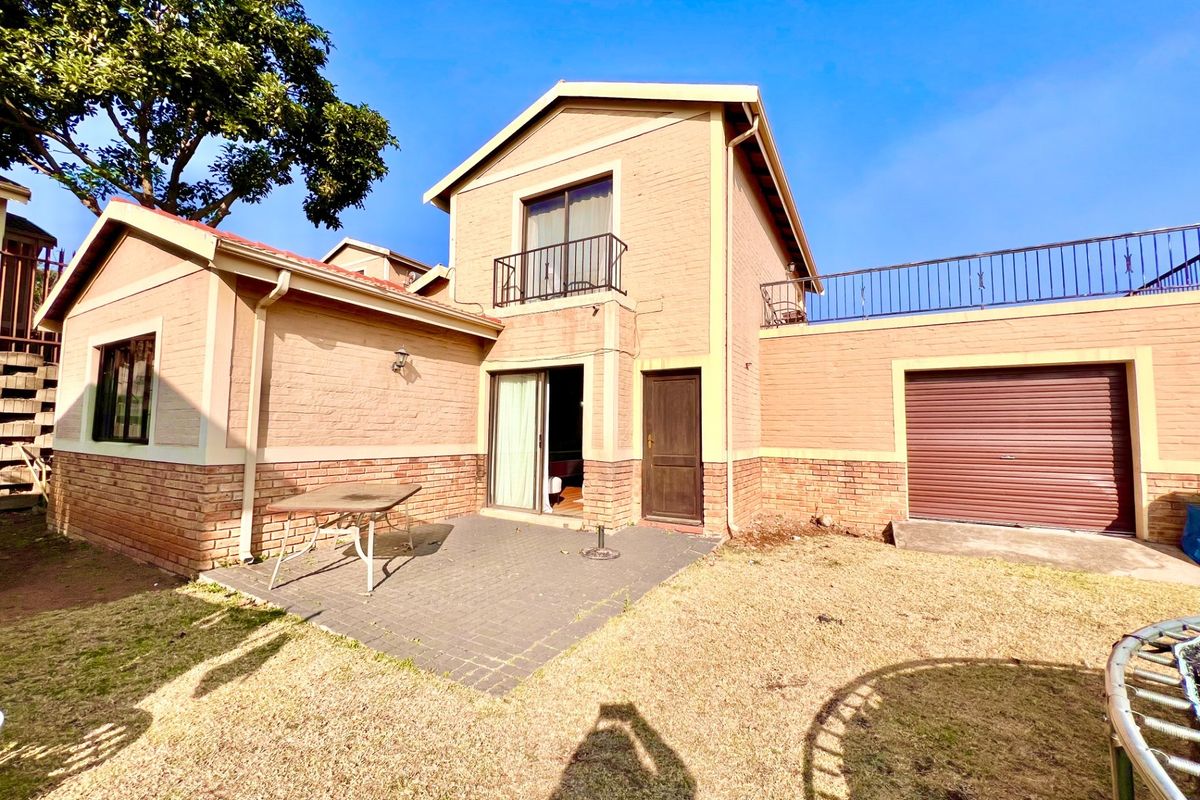 Rear view of a two-story brick house featuring a paved patio area, a balcony, and an integrated garage.