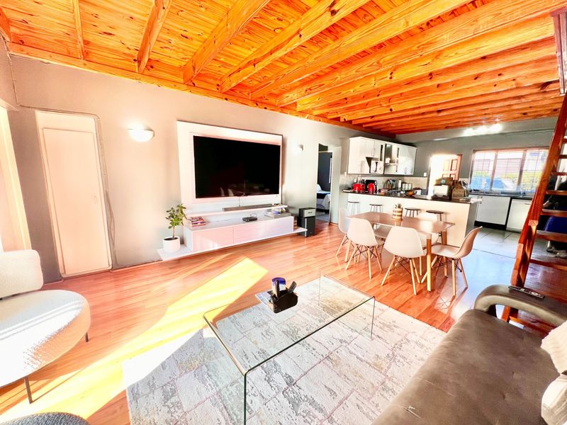Spacious open-plan living and dining area featuring exposed timber beam ceilings, laminate flooring, and a modern kitchen with a central island.