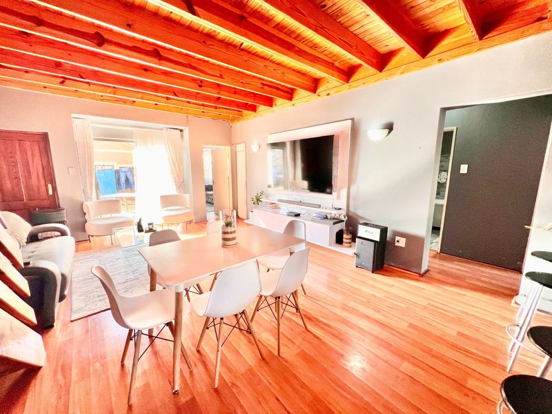 Spacious open-plan living and dining area featuring warm hardwood flooring and a distinctive exposed timber beam ceiling.