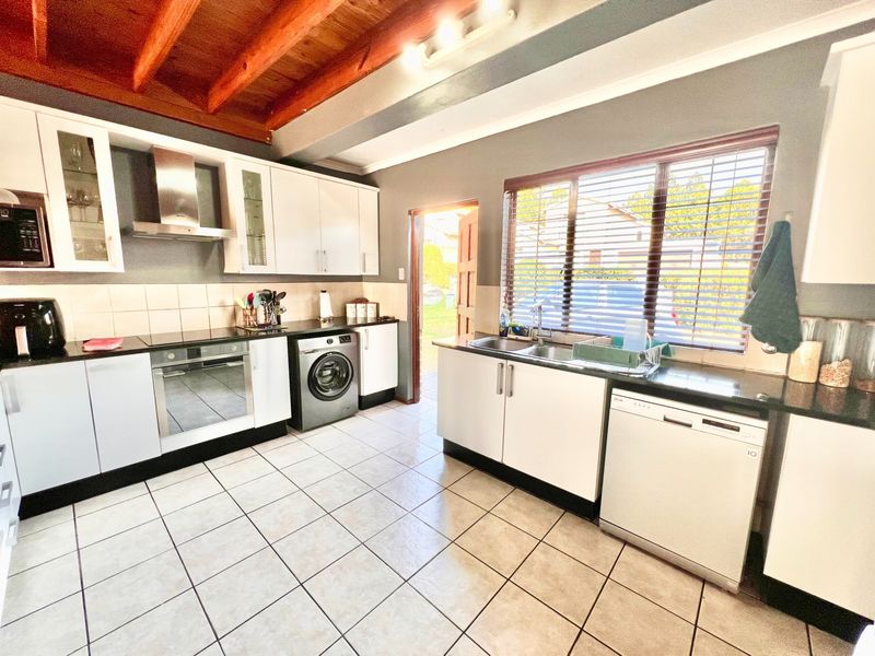 A functional kitchen featuring white cabinetry, granite countertops, built-in oven, extractor fan, and exposed timber ceiling beams with direct access to the rear exterior.
