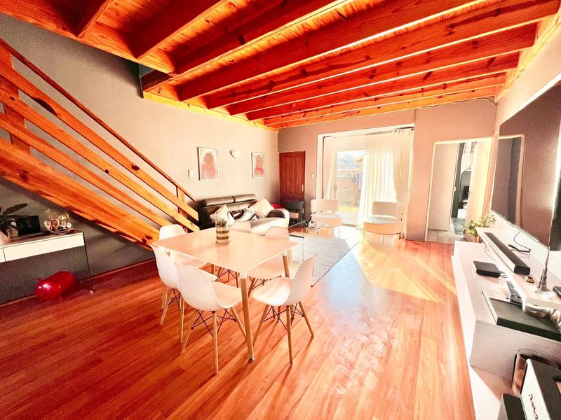 Open-plan living and dining area featuring exposed timber ceiling beams, a wooden staircase, and direct access to the rear patio through sliding glass doors.
