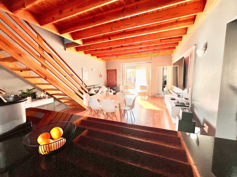 Spacious open-plan living and dining area featuring exposed timber ceiling beams, wooden flooring, and a modern staircase, flowing towards a bright rear patio.