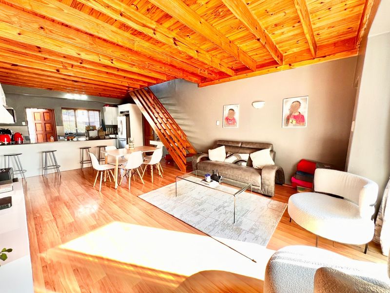 Spacious open-plan living and kitchen area featuring exposed timber beam ceilings, warm laminate flooring, and a central staircase.
