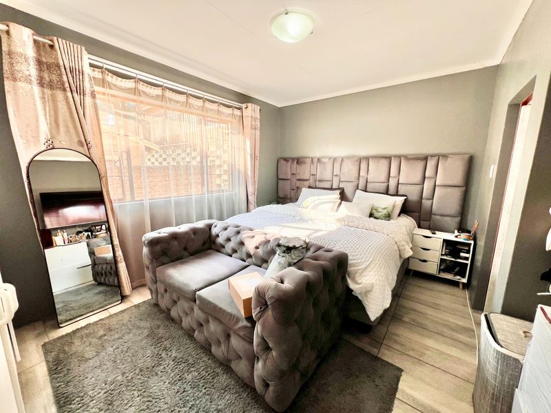 A well-maintained bedroom featuring tiled flooring, a large upholstered headboard, and natural light through a window with curtains.