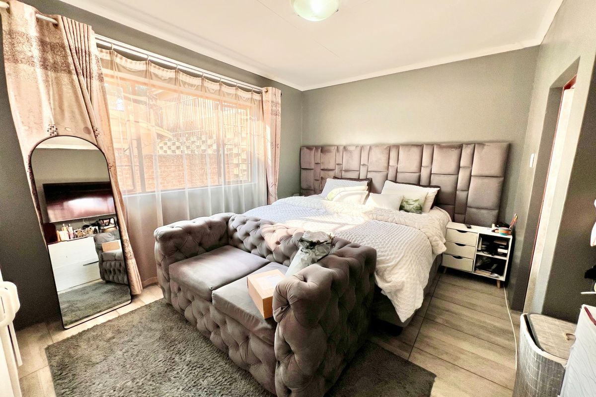 A well-maintained bedroom featuring tiled flooring, a large upholstered headboard, and natural light through a window with curtains.