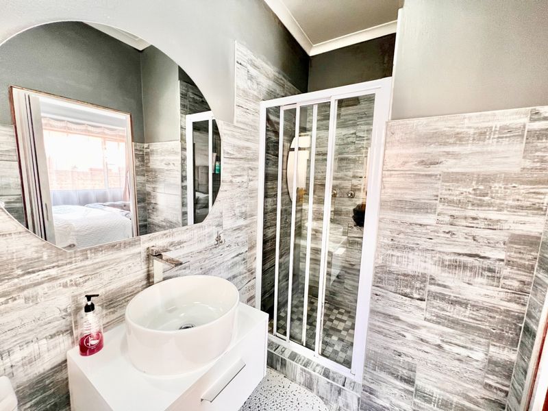 Modern bathroom featuring a vessel sink on a white vanity, wall-mounted faucet, and a glass-enclosed shower with wood-look tiled walls.