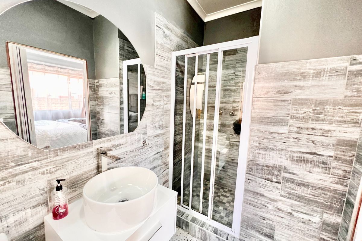 Modern bathroom featuring a vessel sink on a white vanity, wall-mounted faucet, and a glass-enclosed shower with wood-look tiled walls.