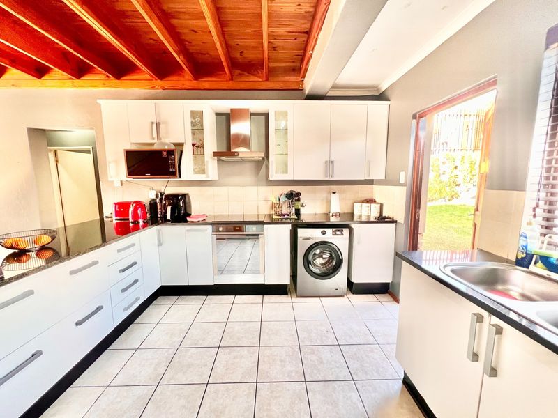 Modern kitchen featuring white cabinetry, granite countertops, stainless steel appliances, and a distinctive exposed timber beam ceiling with direct access to the garden.