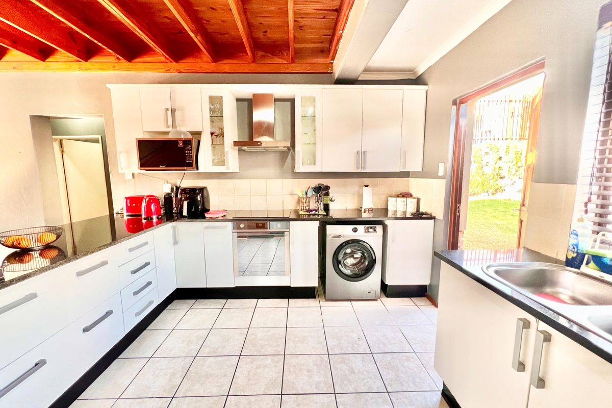 Modern kitchen featuring white cabinetry, granite countertops, stainless steel appliances, and a distinctive exposed timber beam ceiling with direct access to the garden.