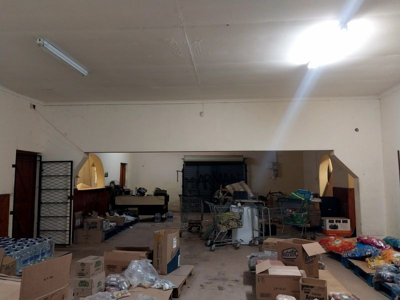 Spacious open-plan retail area featuring high ceilings, a secure roller shutter door, and arched architectural details, requiring cosmetic refurbishment.