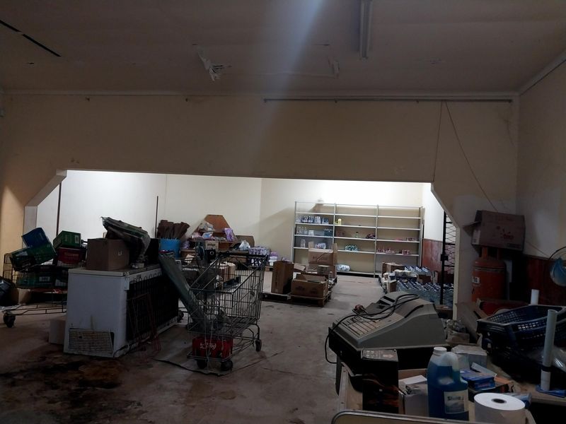 A utility or storage area within a retail space featuring concrete floors, metal shelving, and overhead fluorescent lighting, currently in need of maintenance.