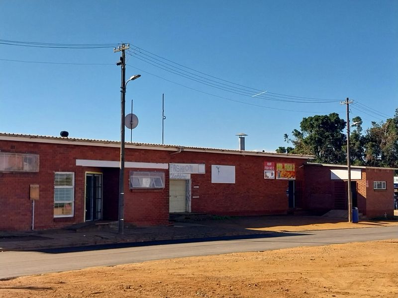 A single-story brick retail building featuring multiple storefront entrances, metal roofing, and exterior signage mounts along a paved road.
