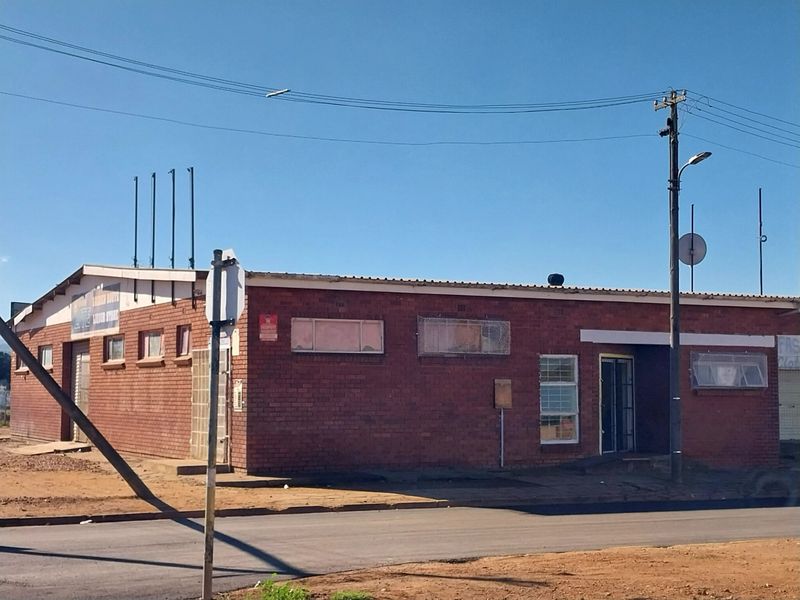 A street-facing view of a single-story brick retail building featuring security bars on windows and a metal roof structure.