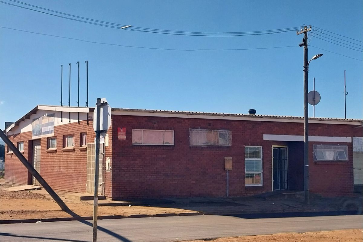 A street-facing view of a single-story brick retail building featuring security bars on windows and a metal roof structure.