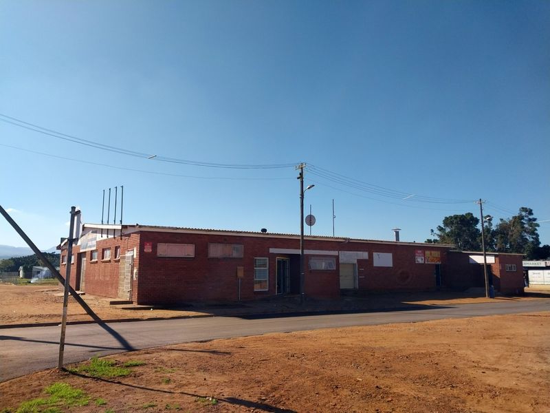 A single-story commercial retail building featuring a face brick exterior, metal roofing, and multiple access points situated along a paved road.