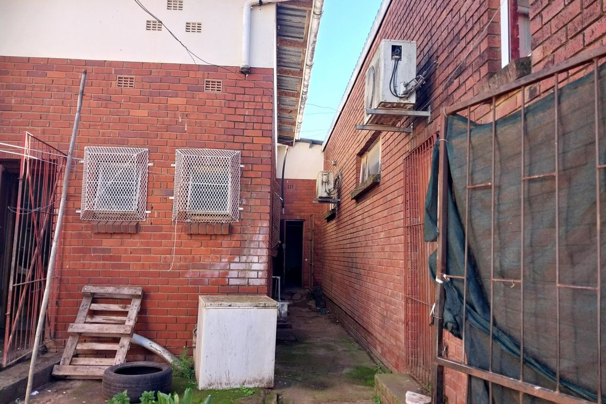 Rear exterior view of the retail property featuring brick walls, security window grilles, and mounted air conditioning units along a narrow paved walkway.