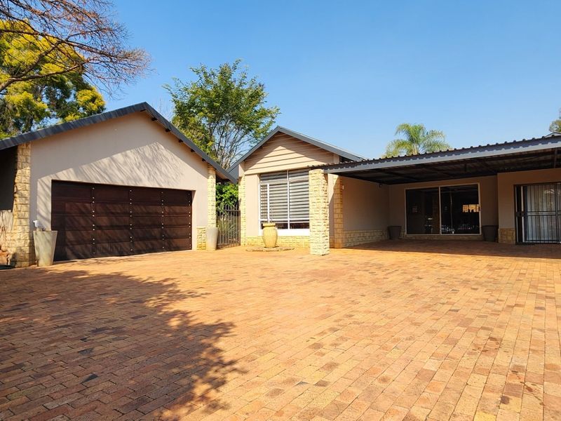 Front exterior view featuring a spacious paved driveway, double garage, and a covered carport area with stone-clad accents.