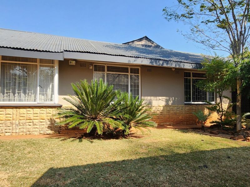 Rear view of the house featuring a corrugated metal roof, stone cladding base, and large windows with security bars overlooking a garden.