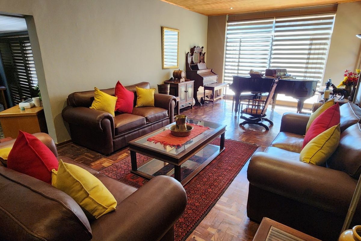 Spacious living room featuring warm parquet flooring, timber ceiling accents, and large windows with fitted venetian blinds, offering a comfortable and traditional atmosphere.