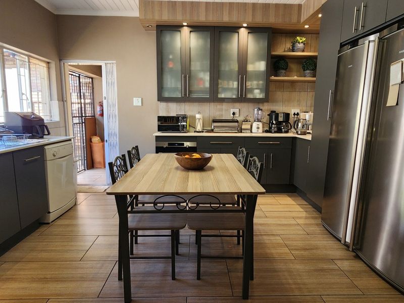 Modern open-plan kitchen featuring dark cabinetry, wood-look tiled flooring, integrated appliances, and ample natural light from large windows.
