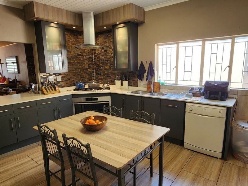 Modern kitchen featuring dark cabinetry, stone countertops, built-in oven with gas hob, stainless steel extractor, and tiled splashback, opening into a living area.