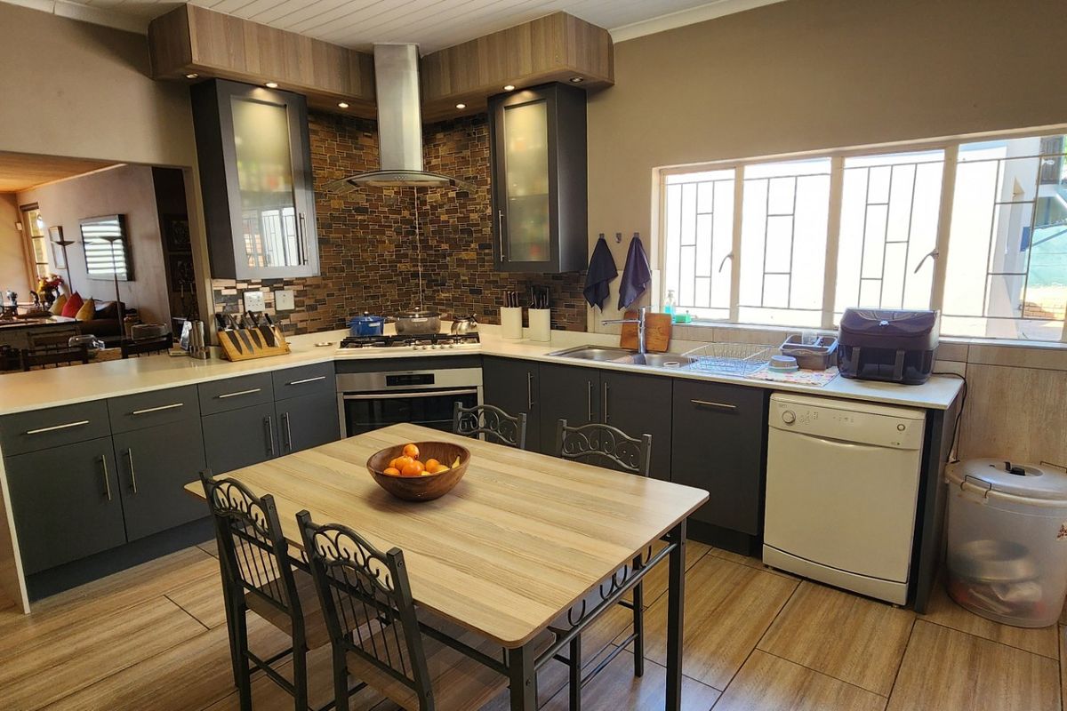 Modern kitchen featuring dark cabinetry, stone countertops, built-in oven with gas hob, stainless steel extractor, and tiled splashback, opening into a living area.