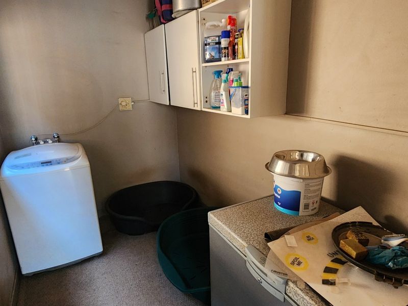 A functional laundry room featuring wall-mounted storage cabinets, a window with security bars, and dedicated plumbing connections for laundry appliances.