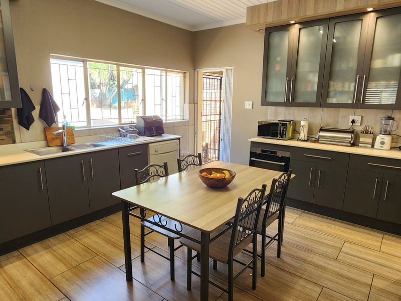 Modern kitchen featuring dark cabinetry, stone countertops, integrated appliances, and a central dining area with tiled flooring and ample natural light.
