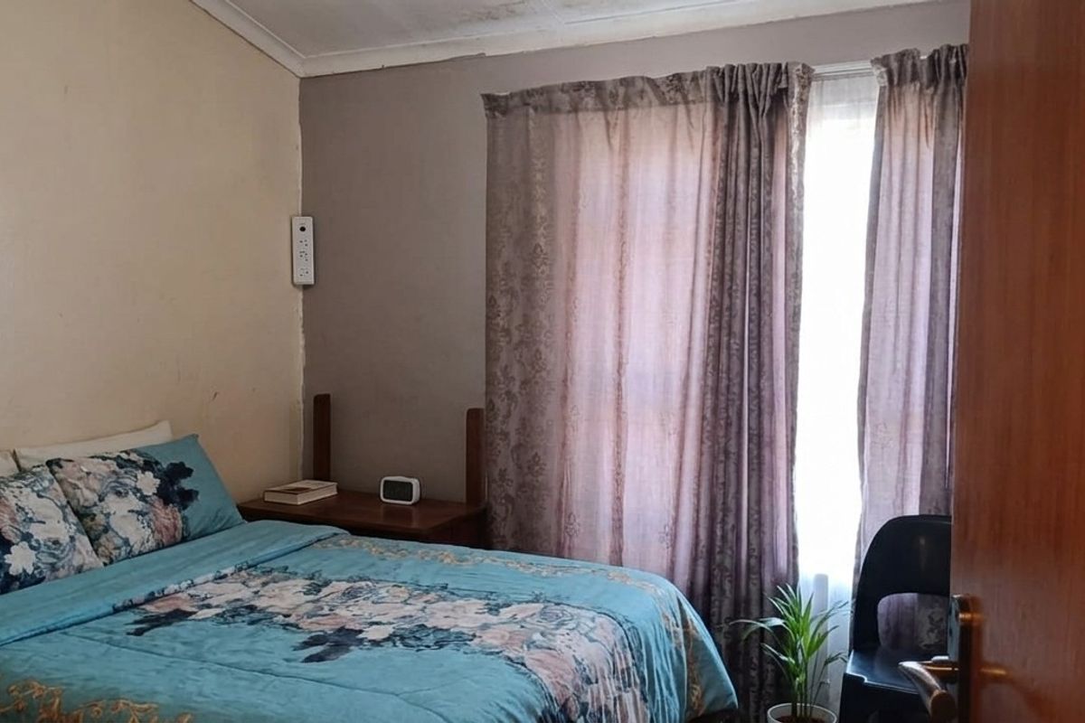 A bedroom featuring a window with curtains and visible signs of ceiling water damage and paint deterioration.