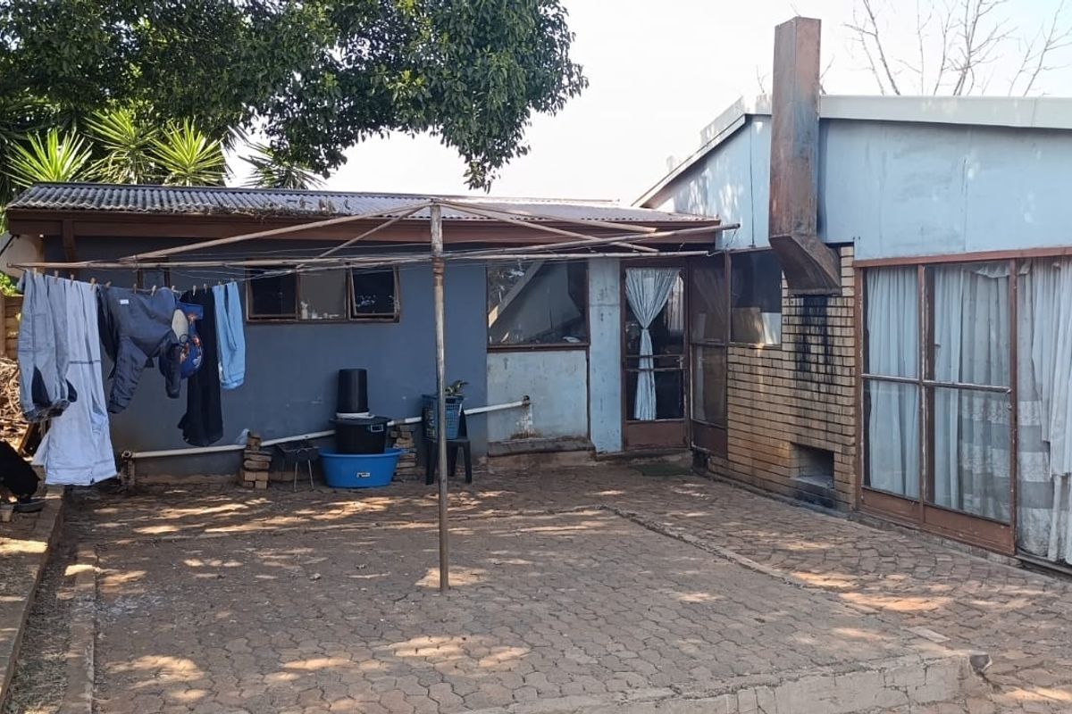 Rear exterior view featuring a paved patio area, built-in braai, and sliding glass doors leading into the home.