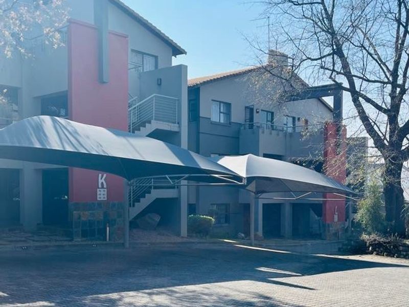 Exterior view of an apartment complex featuring paved parking with shade cloth carports, multi-level balconies, and external staircases.