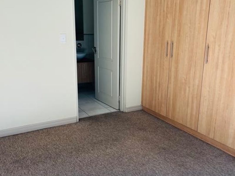A clean, empty bedroom featuring neutral walls, carpeted flooring, and built-in wooden cupboards, with an adjacent view into a bathroom.