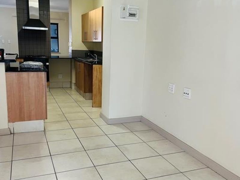 An open-plan kitchen area featuring tiled flooring, wooden cabinetry, a built-in extractor fan, and a kitchen island, presenting a clean and functional layout.