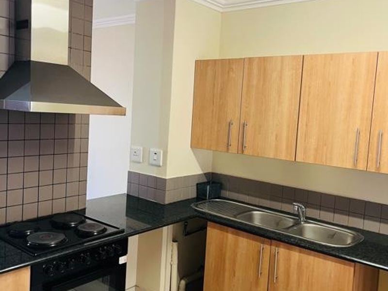 A functional kitchen featuring laminate cabinetry, granite countertops, a stainless steel extractor fan, and a built-in oven, with an open space under the sink.