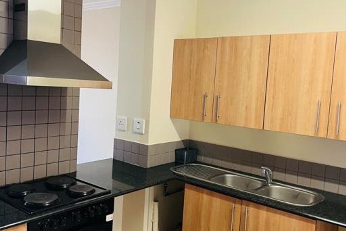 A functional kitchen featuring laminate cabinetry, granite countertops, a stainless steel extractor fan, and a built-in oven, with an open space under the sink.